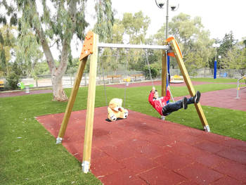 A boy swing on the swing set with a teddy bear placed on the swing next to him